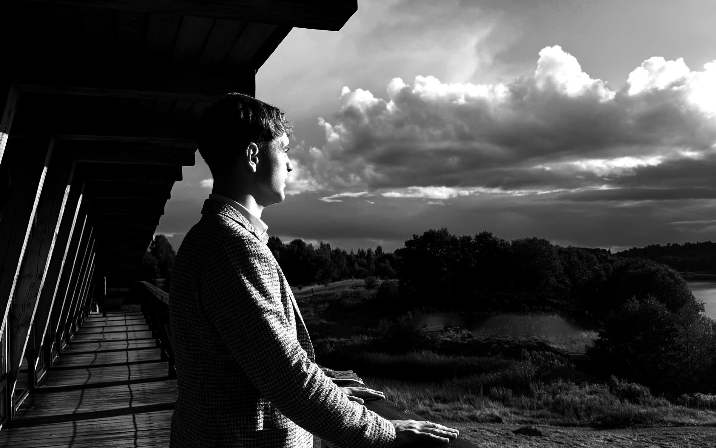 Ivas in profile on a wooden gallery, looking out over open land